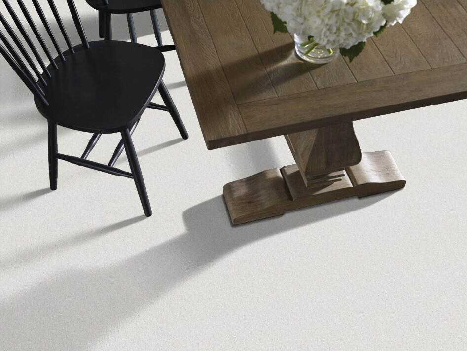 A top-down view of a rustic wooden trestle table with a black spindle-back chair and a vase of white flowers on a light beige textured floor.