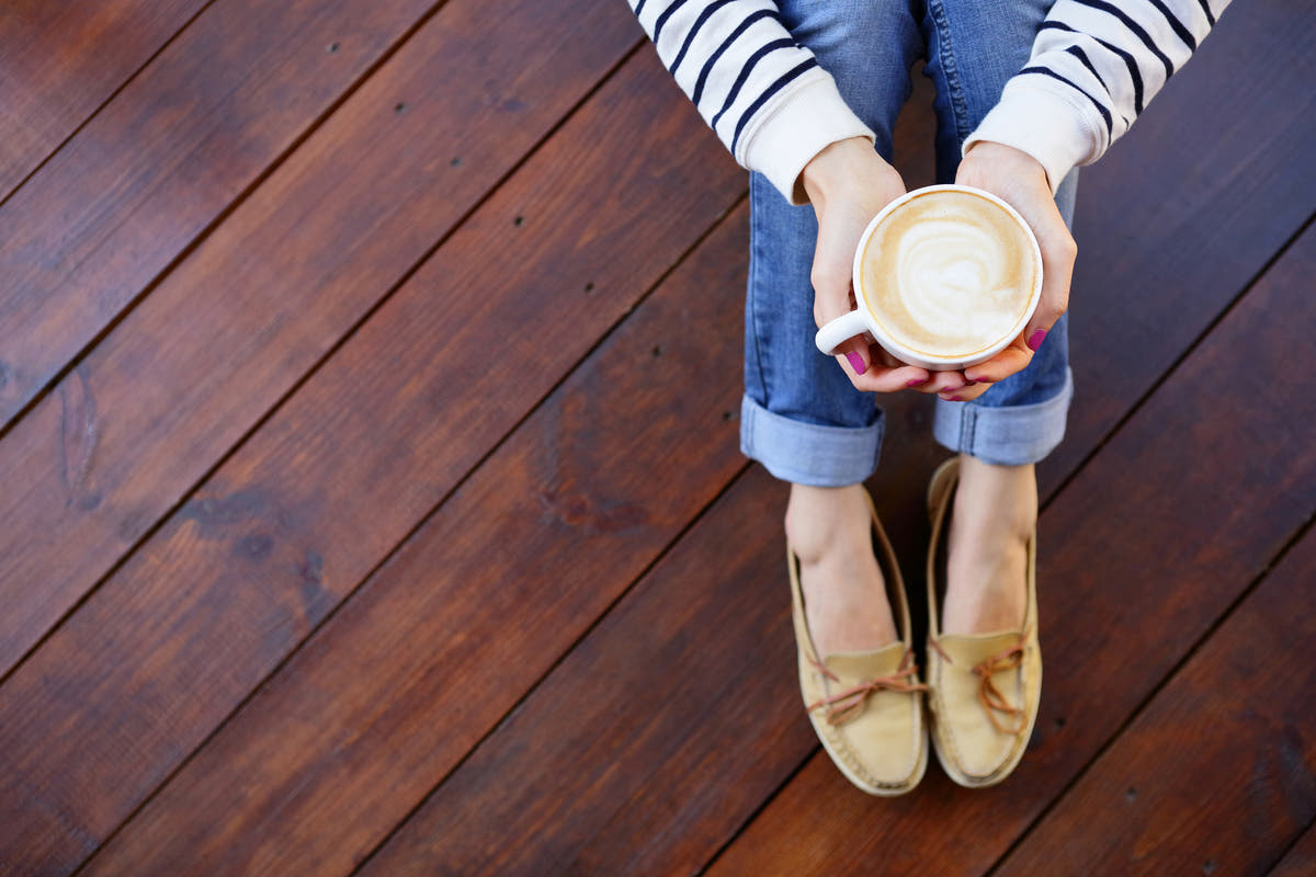 Person holding a cup of coffee on a wooden floor